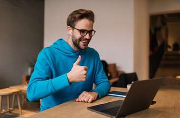 Wall Mural - Happy male blogger have influence live stream for communicate with network followers using laptop computer and front web camera in coworking, smiling man in spectacles and earbuds make video calling