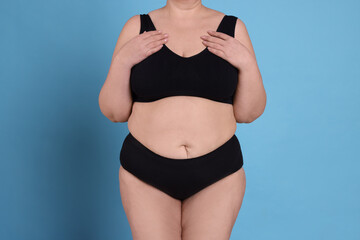 Wall Mural - Overweight woman in underwear on light blue background, closeup