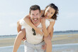man giving piggyback ride to girlfriend at the beach