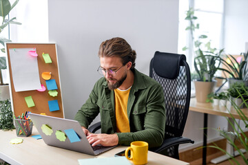 Pleasant caucasian man sit alone in office behind desk working online on laptop, typing on keyboard. handsome guy in casual wear concentrated and focused, planning projects. management concept