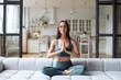 Beautiful healthy woman on the sofa in the lotus position meditates with her eyes closed.