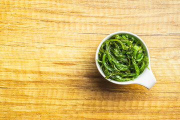 Wall Mural - Green wakame. Seaweed salad in bowl on wooden table.