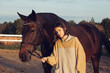 A young girl with a short haircut next to her horse at sunset. Good friends. Summer and happiness.