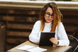 © Алина Битта - Young female student in glasses sitting at the table, using tablet when studying or working at cafe,using computer. Freelance business woman or student, blogging, studying, shopping, making notes.