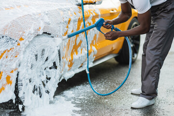 Wall Mural - Car washing outdoors. Crop close up of car washing high pressure foam. Wheel alloy cleaning at car wash station with high pressure foam. Washing rims.