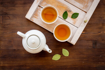 Wall Mural - Black tea in cups with white teapot and green leaves