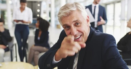 Wall Mural - Mature businessman in an office with his colleagues in the background. Mature caucasian businessman smiling happy talking and pointing his finger making a gesture sitting at work.