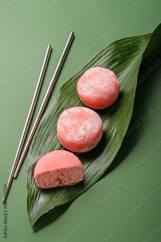 Delicious mochi, leaf and chopsticks on color background