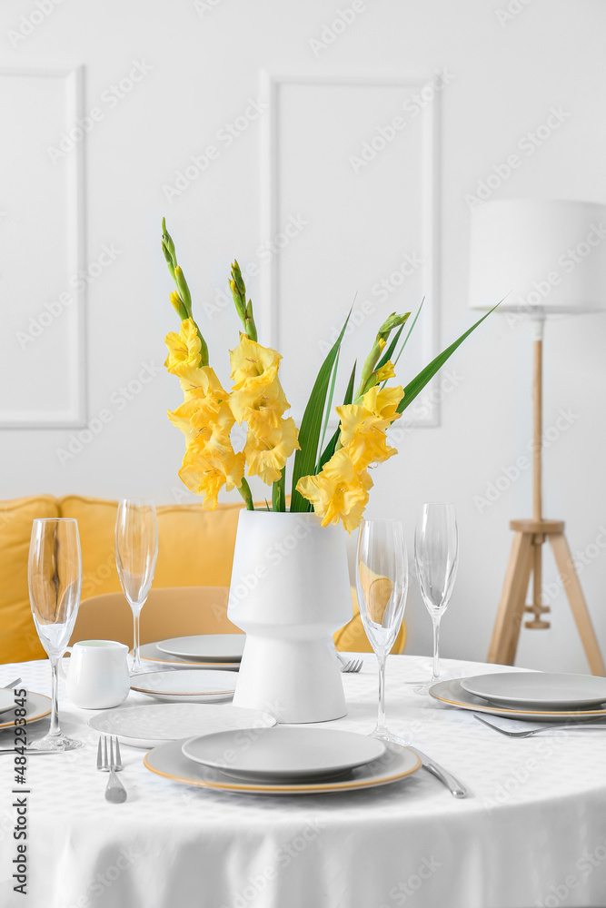 Vase with beautiful Gladiolus flowers on served table in light room