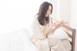 © lielos - 寝室のベッドに座り携帯電話を見ている女性