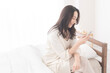 © lielos - 寝室のベッドに座り携帯電話を見ている女性