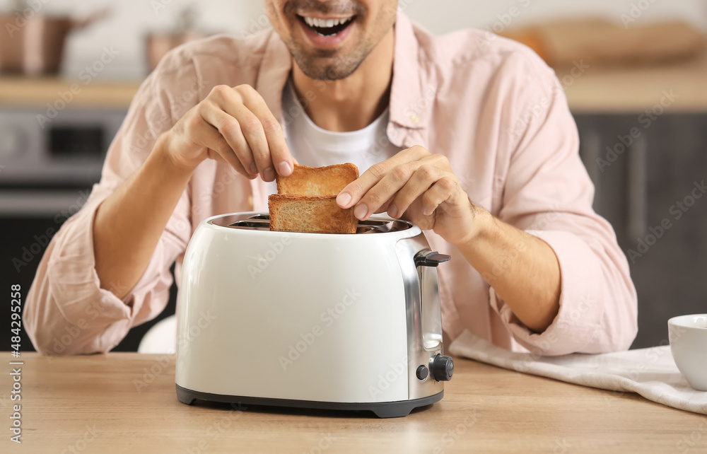Young man making tasty toasts in kitchen