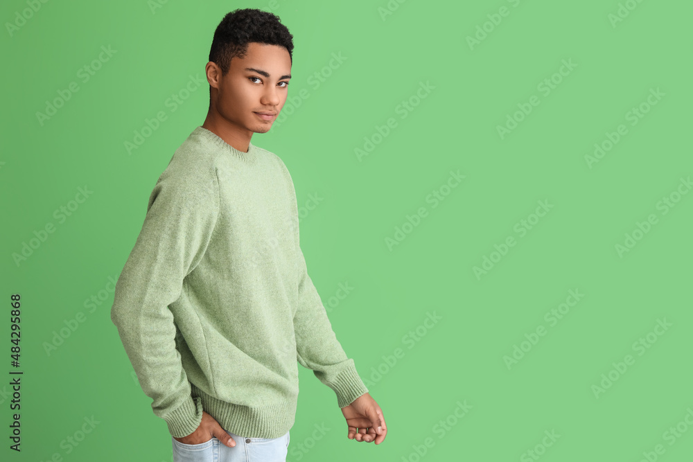 Handsome African-American guy in knitted sweater on color background