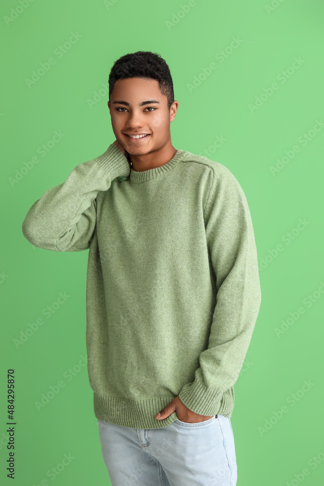 Handsome African-American guy in knitted sweater on color background