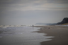 A View Of The Sandy Beach And Waves Washing The Coast And A Lonely Man Standing