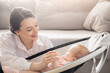 Mom holds little infant daughter by hand in automatic cradle for sleeping, sun light. Concept Morning with newborn baby