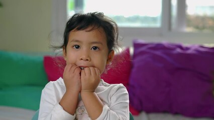 Wall Mural - Little Asian girl biting fingernails while looking to camera. Concept of bad habits. 4K Slow motion.