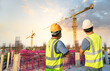 Asian engineer manager and foreman or leader discussion pointing to construction site project on workplace construction building structure and crane in the background.concept of Teamwork, Leadership