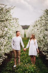 Wall Mural - Beautiful young couple in a romantic place, spring blooming apple orchard. Happy joyful couple enjoy each other while walking in the garden. Man holding woman's hand