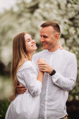 Wall Mural - Young loving couple in a walk in a spring blooming apple orchard. Happy married couple enjoy each other while walking in the garden. Man holding woman's hand