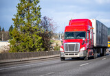 Fototapeta Mapy - Bright red big rig semi truck transporting cargo in semi trailer running on the turning highway road