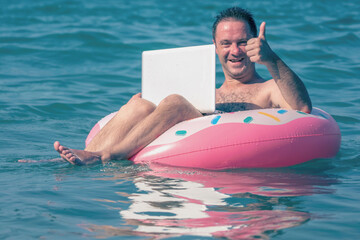 Working anywhere and any time concept. Very happy man freelance businessman working at laptop on inflatable ring in the water of sea.