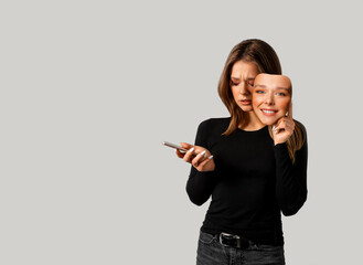 Portrait of a sad girl with a smartphone in one hand and a smiling mask in the other hand.