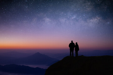 Wall Mural - Silhouette of young couple of lovers watched the star, milky way, night sky on top of the mountain. They enjoyed traveling and was successful when he reached the summit.