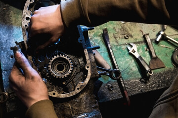 Mechanic with oily hands doing repairs in dark workshop, close up, soft selective focus. Man disassembled engine.