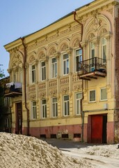 Wall Mural - Rostov-on-Don, Russia - September 12, 2019: Facade old two-story building on Donskaya Street. On balcony gypsy woman hangs sheets for drying. On street in front building, piles of sand and dug pits.