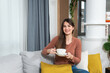 © Srdjan - Portrait of joyful young woman enjoying a cup of coffee at home. Smiling pretty girl drinking hot tea in winter. Excited woman enjoying her day off work relaxing at cozy warm modern studio apartment.