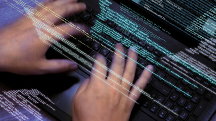 Programmer at work - Caucasian man hands typing on laptop keyboard, elements of software code running on screen and flying in the air. Hacker or coder working with notebook. 