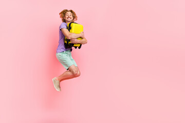 Wall Mural - Full length body size view of attractive cheery guy jumping hugging bag low cost airline isolated over pink pastel color background