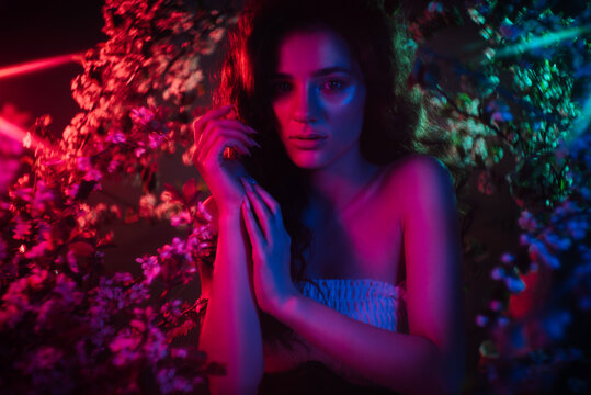 A fantastic shot of a girl in flowers with neon multicolored light and phantasmagoria. The concept of fantasy, fairy tales, magic and fairies.