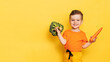 A studio shot of a smiling boy holding fresh broccoli and carrots on a yellow background. The concept of healthy baby food. Place for your text