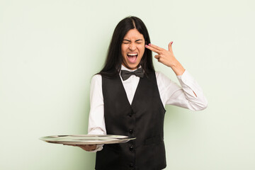 Wall Mural - young pretty hispanic woman looking unhappy and stressed, suicide gesture making gun sign. waiter with tray concept