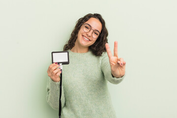 Wall Mural - young pretty hispanic woman smiling and looking friendly, showing number two. accreditation card id