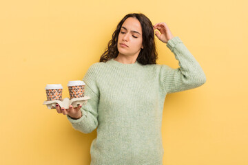 Wall Mural - young pretty hispanic woman feeling puzzled and confused, scratching head. take away coffee concept