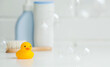 Baby bath accessories. Child care. Miniature yellow rubber duckling for bathing with a brush and shampoo bottles. Soap bubbles, bath foam.