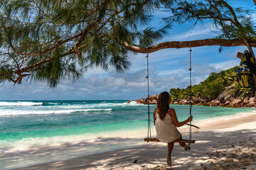 Young woman on a swing on a sandy beach. Idyllic turquoise water with splashing waves. Exotic tourist and travel destination on Seychelles