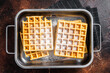 Viennese waffles with powdered sugar in kitchen steel tray. Dark background. Top view