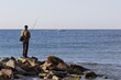 fishing a fisherman stands on the rocks with a spinning rod on the seashore
