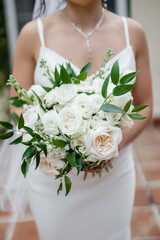 Wall Mural - Beautiful white wedding bouquet of flowers in hands of the Bride holding an elegant bouquet made of white peonies and greenery Cropped photo	