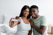 © Prostock-studio - Cheerful young black woman and guy show pregnancy test, sits at bed in bedroom interior