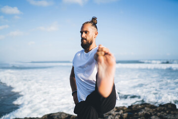 Bearded male yogi stretching body during morning training at seashore enjoying healthy and sportive lifestyle, Caucasian man meditate during hatha practice for holistic healing and retreat