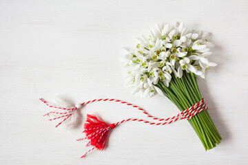 A bouquet of snowdrops flowers, red and white rope with tassels on a wooden background. Postcard for the holiday of March 1, space for text.