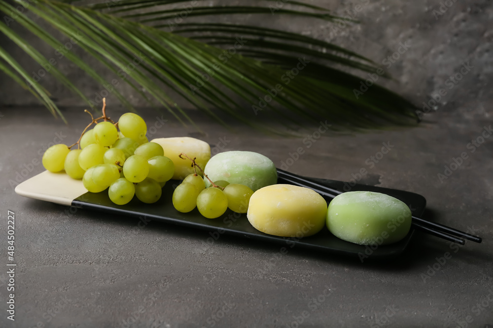 Board with delicious mochi, grape and chopsticks on table