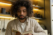 © Grustock - Young focused Muslim man with dark kinky hair in white shirt reads book with recipes in modern kitchen at home close view