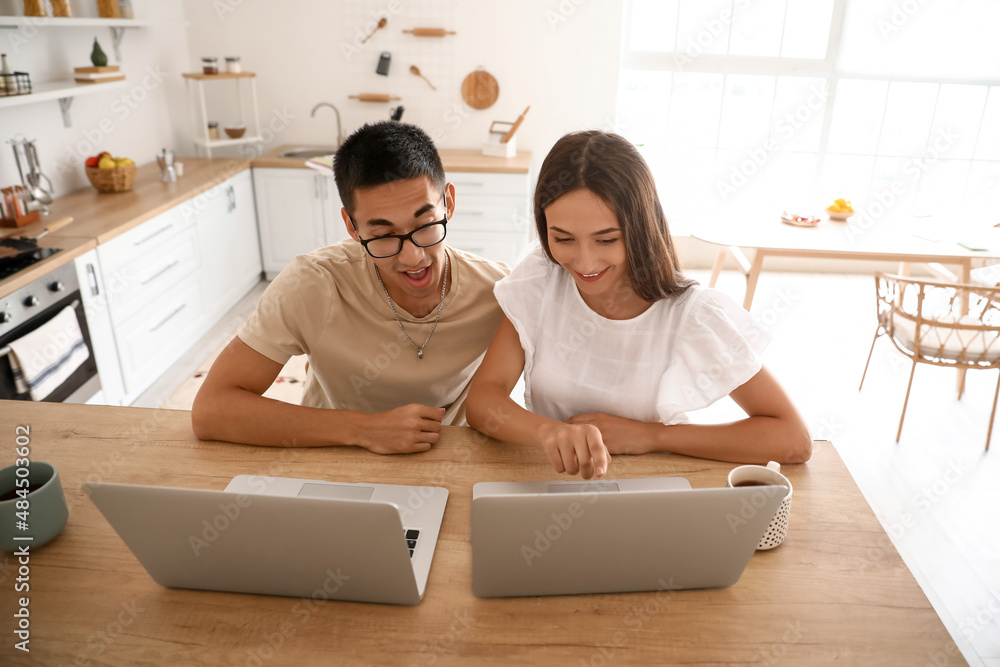 Young woman with her husband using laptops at table in kitchen