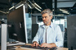 © Liubomir - Experienced worker gray-haired businessman works at the computer in a modern office